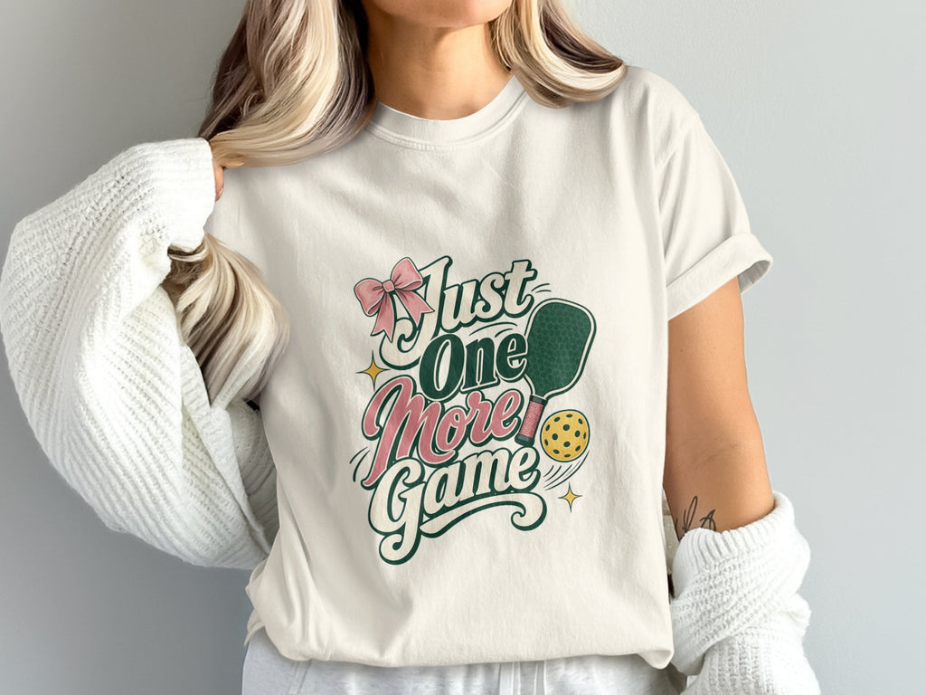 Cream t-shirt with text "Just One More Game", pickleball paddle and ball.