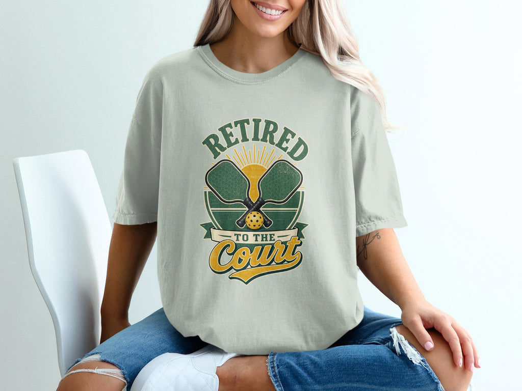 T-shirt graphic reading "Retired To The Court" with pickleball paddles and sun graphic.