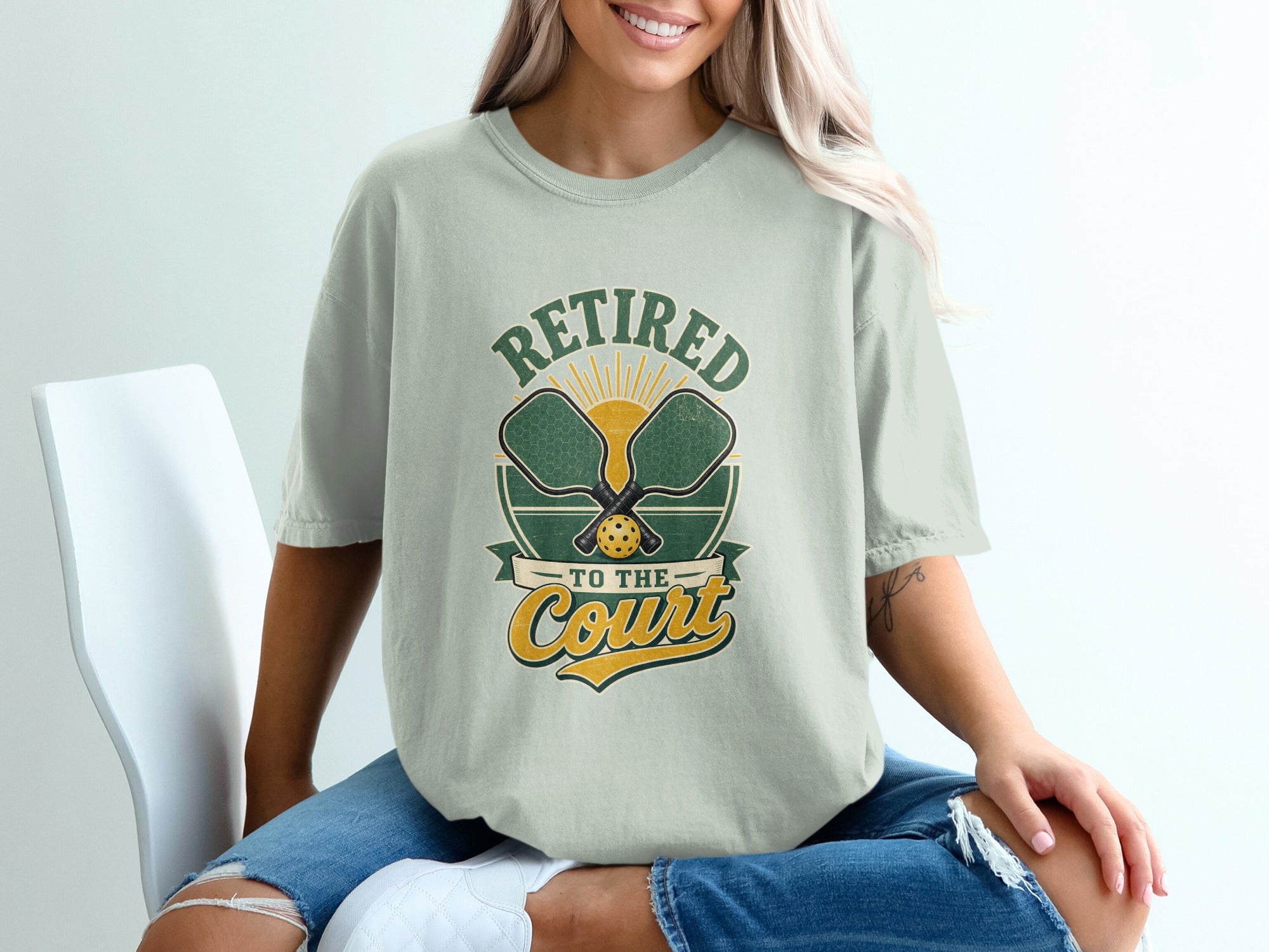 T-shirt graphic reading "Retired To The Court" with pickleball paddles and sun graphic.