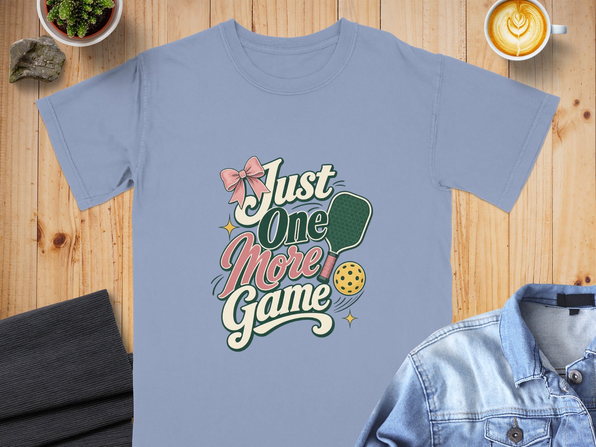 Light blue t-shirt featuring "Just One More Game" with pickleball graphic and pink bow.