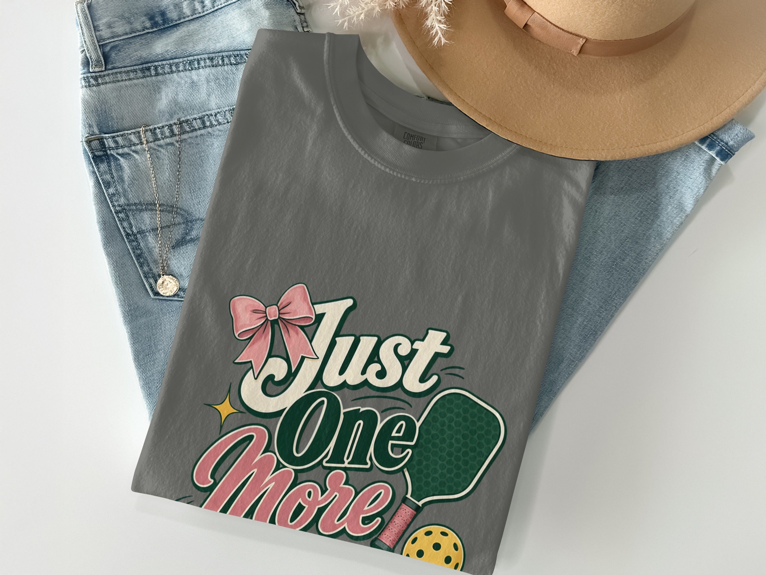 Grey t-shirt with "Just One More" text, pickleball paddle, ball, and bow graphic.