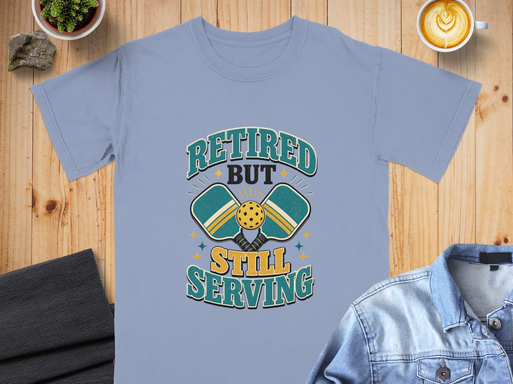 Light blue t-shirt with "Retired But Still Serving" pickleball graphic.