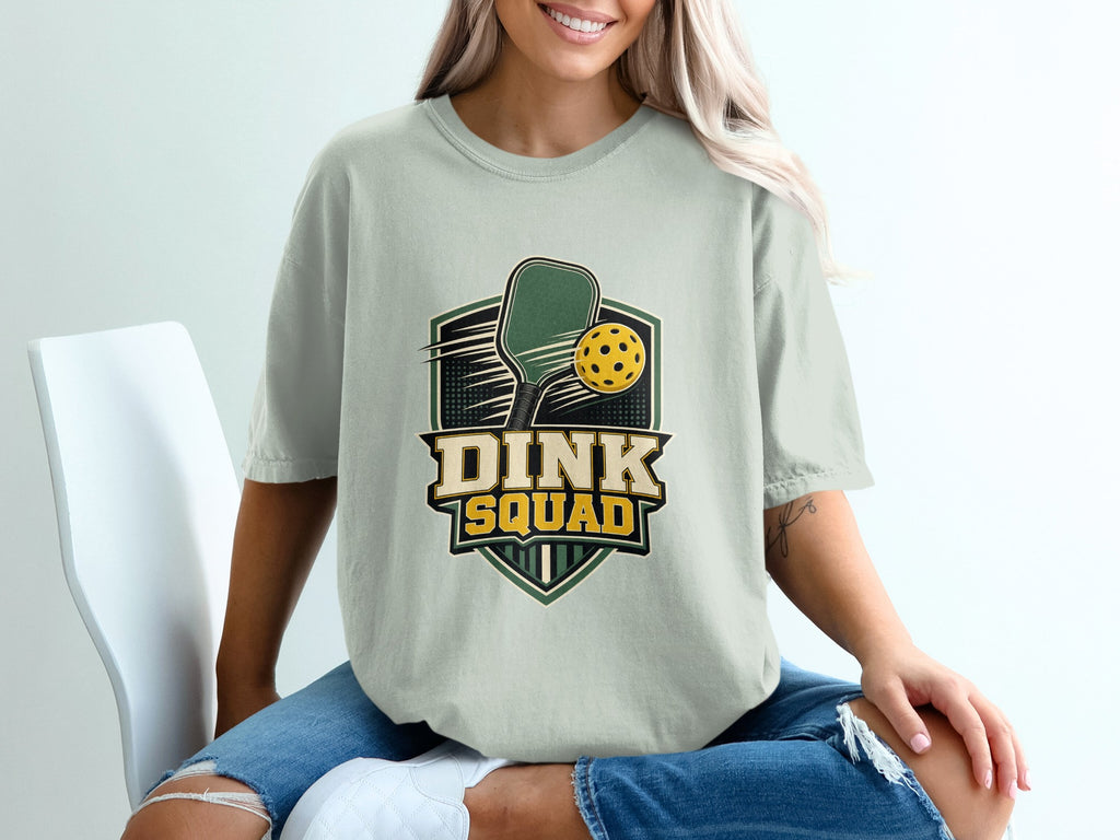 Light green t-shirt with "DINK SQUAD" text over pickleball paddle and ball graphic.