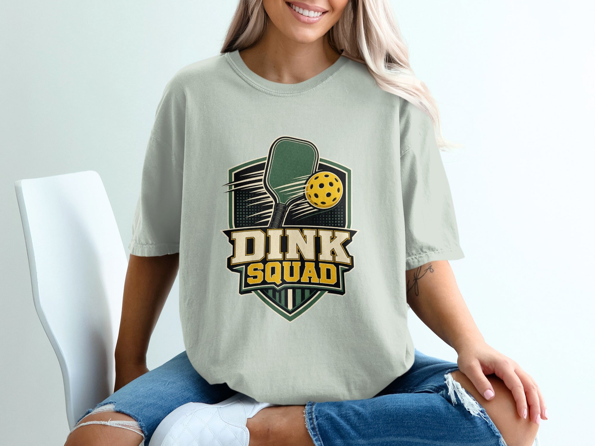 Light green t-shirt with "DINK SQUAD" text over pickleball paddle and ball graphic.