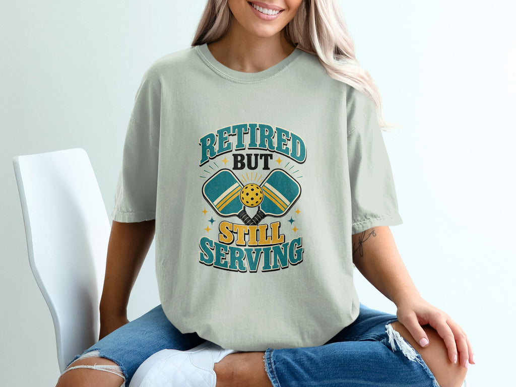 T-shirt graphic: Retired but still serving with pickleball paddles and ball.